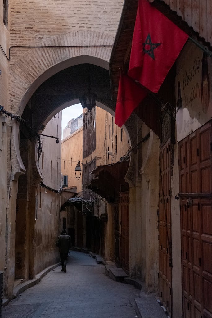 Narrow alleyway in Fez Medina with Moroccan flag and arched architecture.